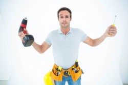 Confused technician holding screwdriver and drill machine